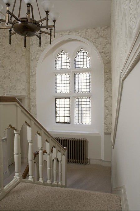 the stairs lead up to an arched window and chandelier in a white room