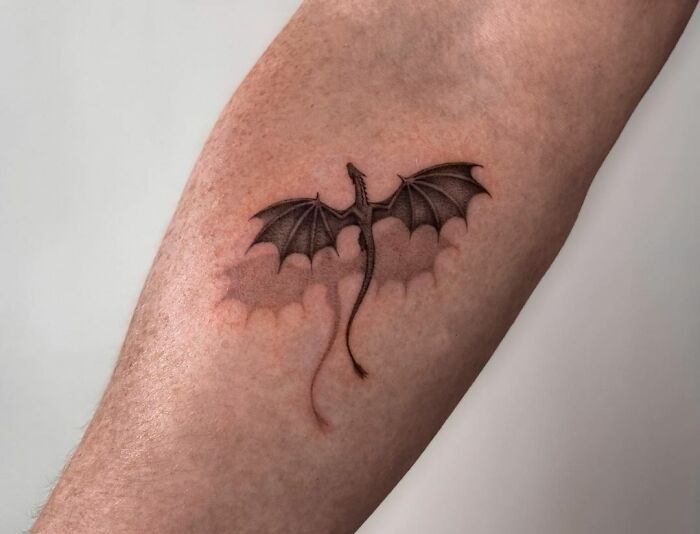 a tattoo on the leg of a man with a dragon wing in it's claws