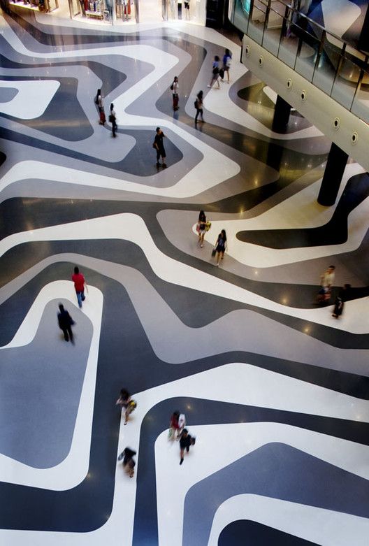 many people are walking around in a large room with black and white designs on the floor