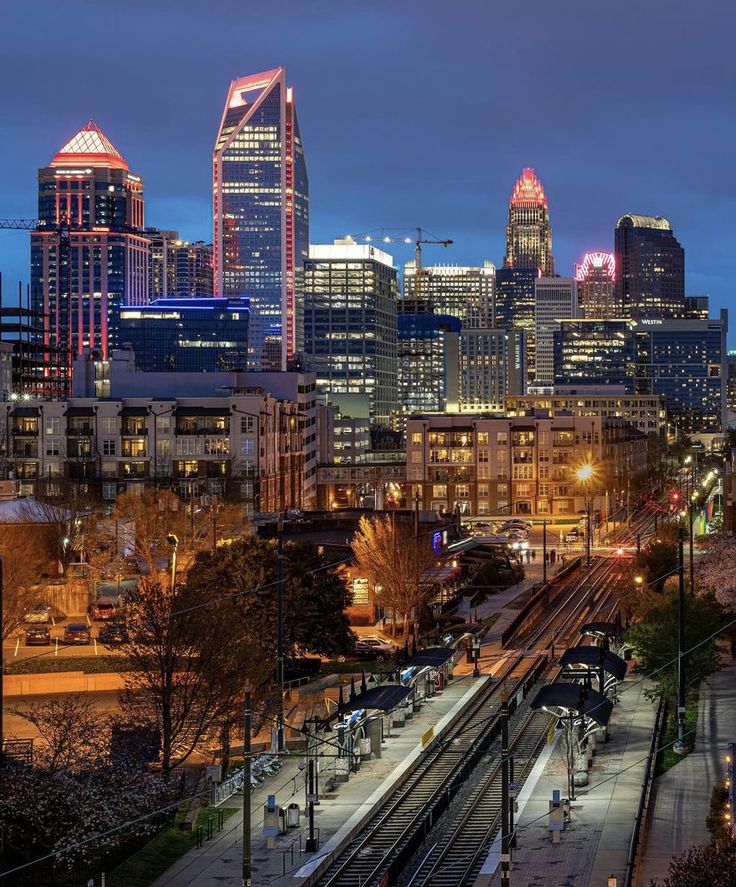 the city skyline is lit up at night, with train tracks running through it and buildings in the background