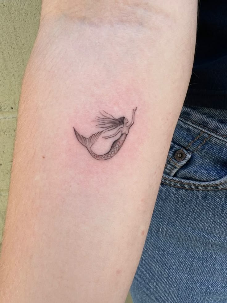 a woman's arm with a small fish tattoo on the left side of her arm