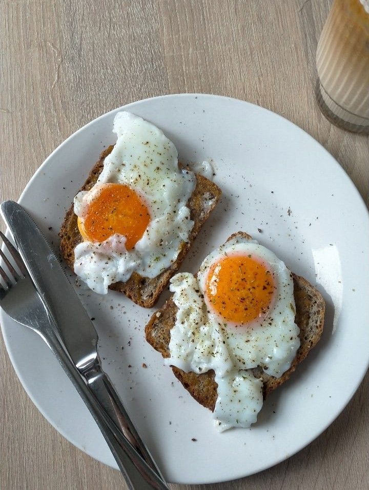 two pieces of toast with eggs on top and a fork next to it, sitting on a white plate