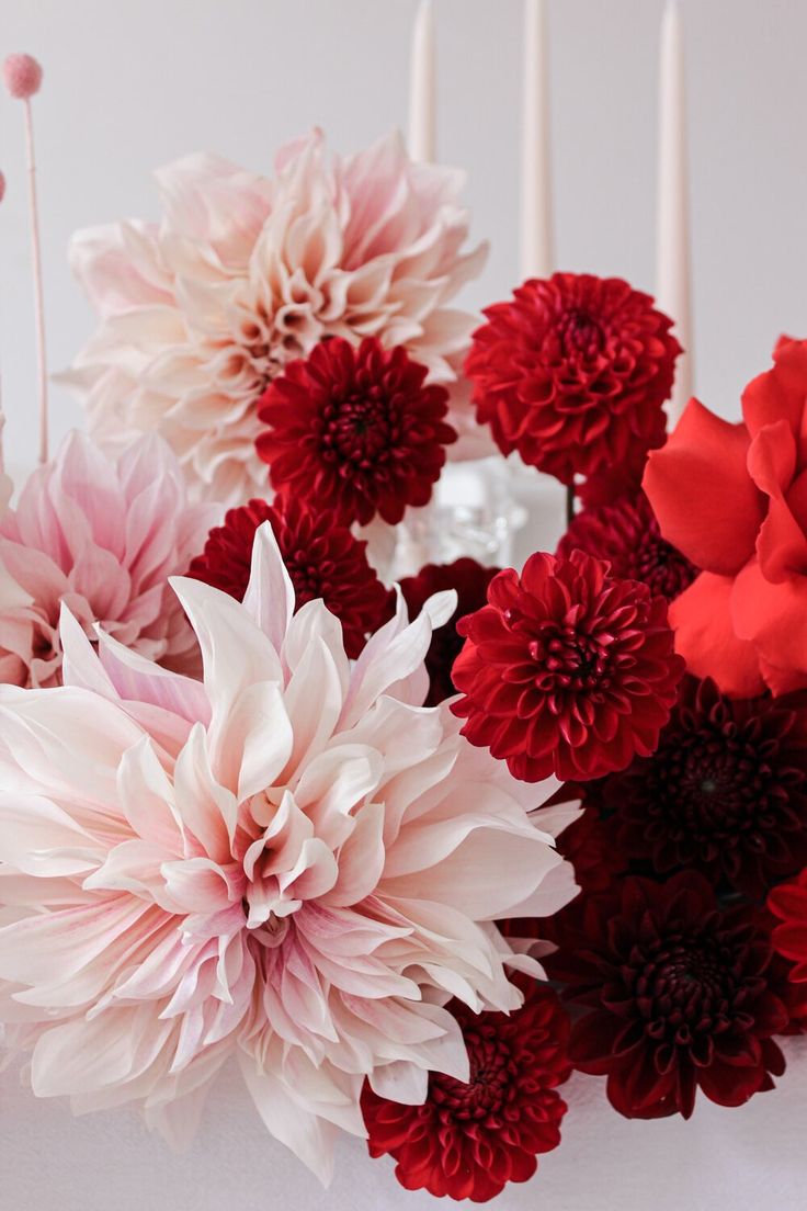 red, pink and white flowers are arranged next to candles