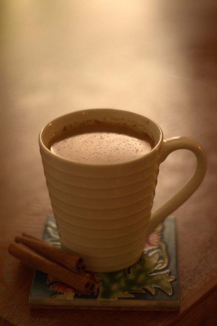 a cup of hot chocolate sitting on top of a table next to two cinnamon sticks