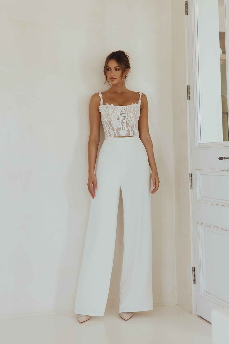 a woman standing in front of a white wall wearing a crop top and wide legged pants