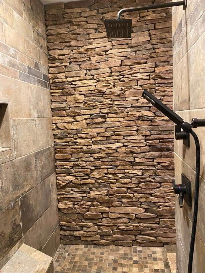 a walk in shower sitting next to a stone wall and tiled floored bathroom area