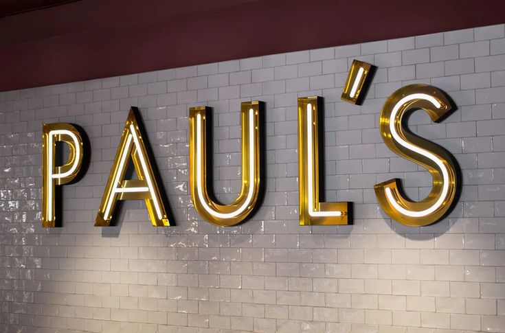 the word paul's is illuminated in gold letters on a white brick wall behind it