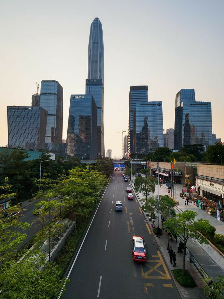 cars are driving down the street in front of tall buildings and skyscrapers at sunset