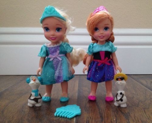 two dolls standing next to each other on a wooden floor