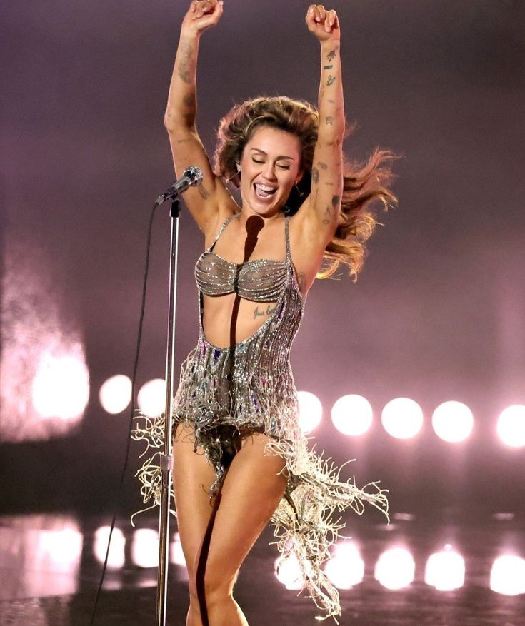 a woman is dancing on stage with her arms in the air and holding a microphone