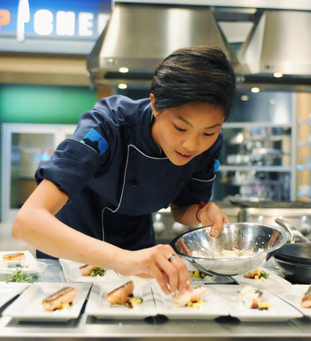 a woman in a kitchen preparing food on top of white plates and pans with utensils