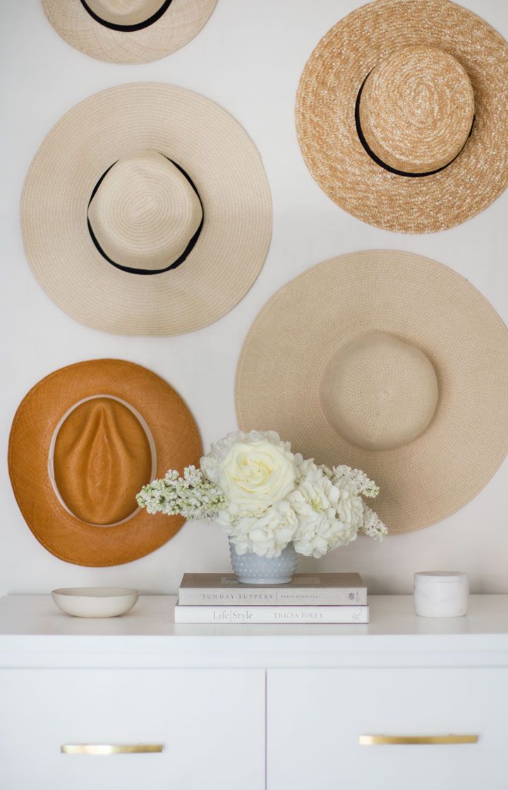 hats are hanging on the wall above a vase with flowers