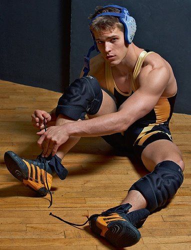 a young man sitting on the floor wearing knee pads and holding a pair of headphones