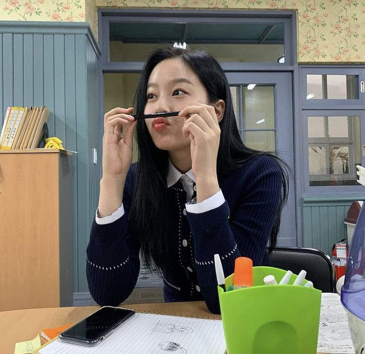 a woman sitting at a table with a pen in her mouth