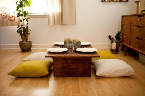 a living room filled with furniture and a wooden coffee table surrounded by pillows on the floor