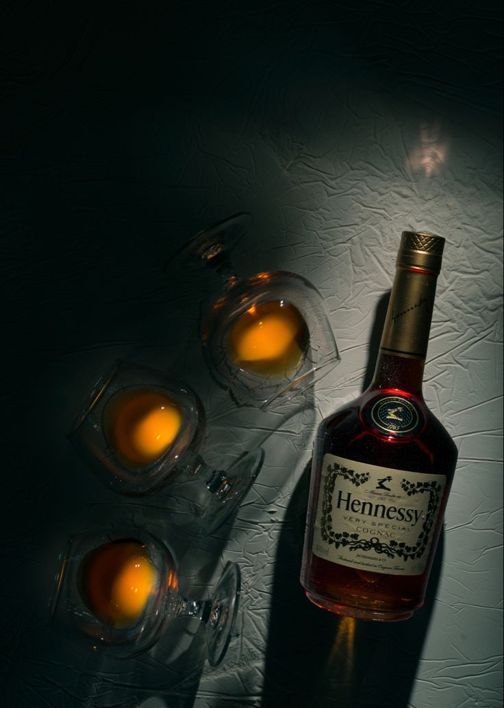 a bottle of hennesy next to some glasses on a table with light coming from behind it