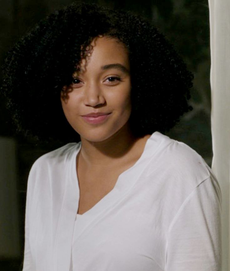 a close up of a person wearing a white shirt and black hair with an afro