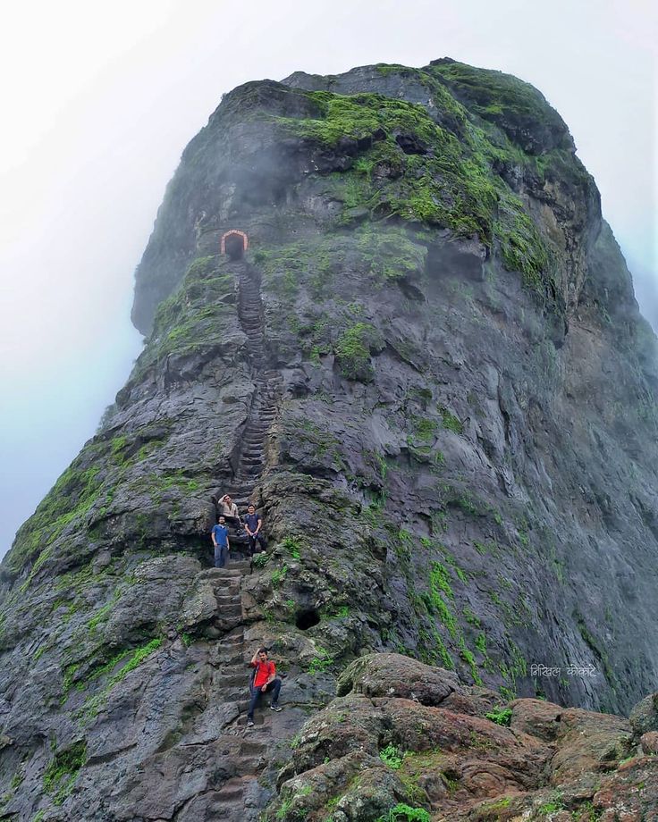 two people climbing up the side of a mountain on a foggy day with stairs