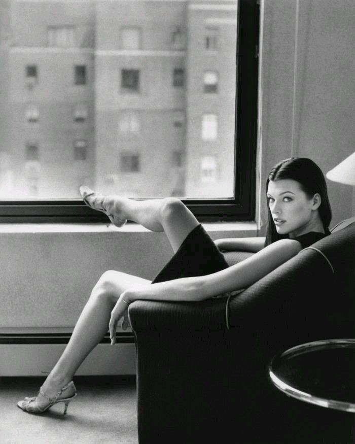 a woman sitting in a chair next to a window with her feet up on the armrest