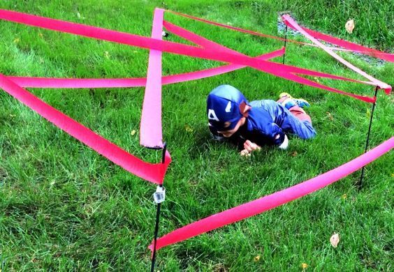 a small child in blue jacket playing with pink tape on grass next to red poles