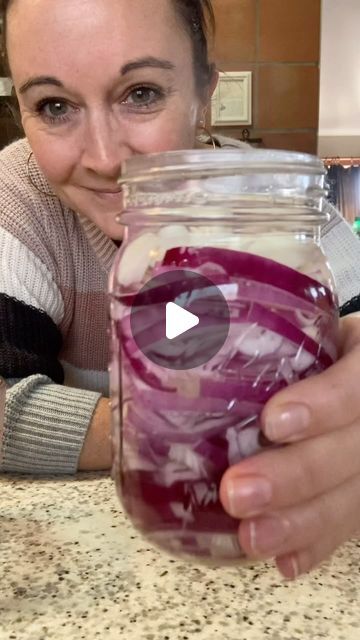 a woman holding a jar filled with red onions