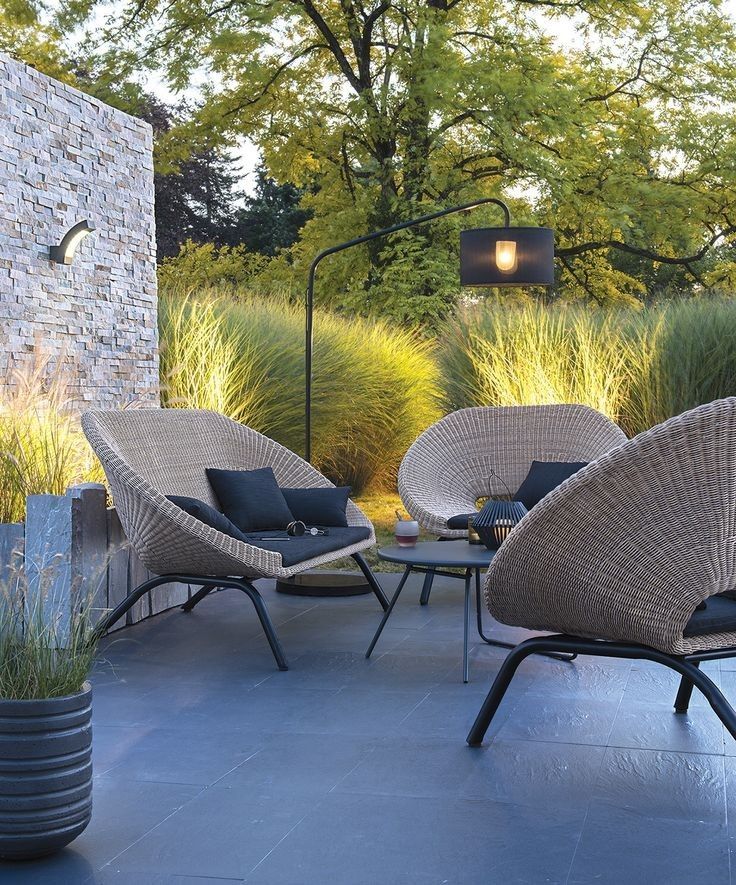 an outdoor patio with wicker furniture and plants in the back ground, next to a stone wall