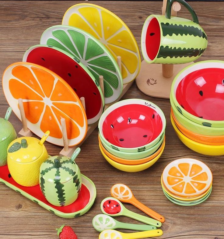 a wooden table topped with lots of colorful plates and bowls filled with fruit like items