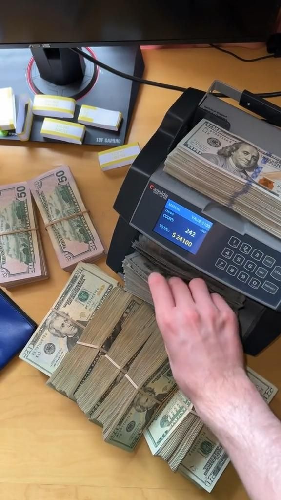 a man is counting money in front of a printer on a desk with other items