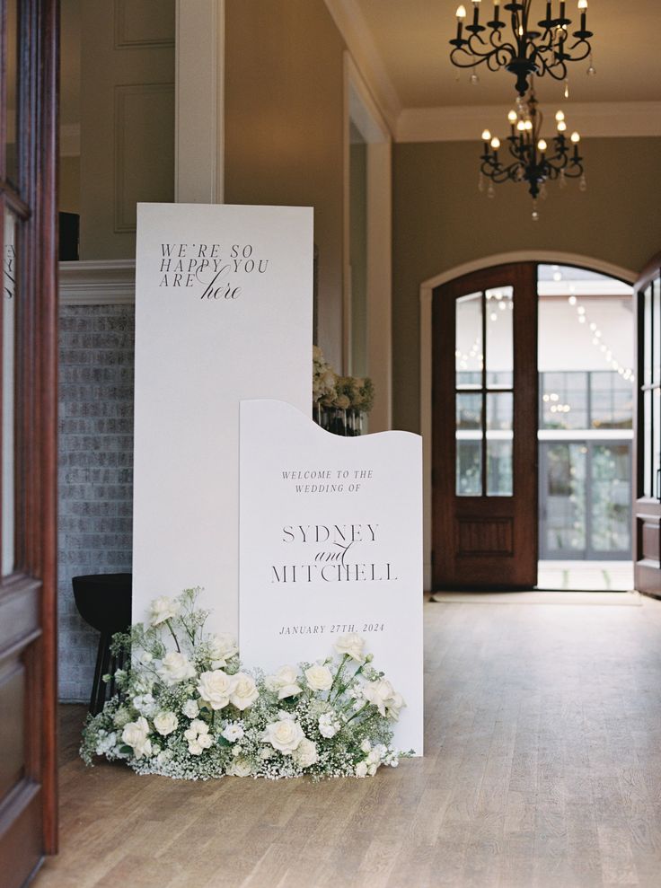 a white sign sitting on top of a wooden floor next to a chandelier