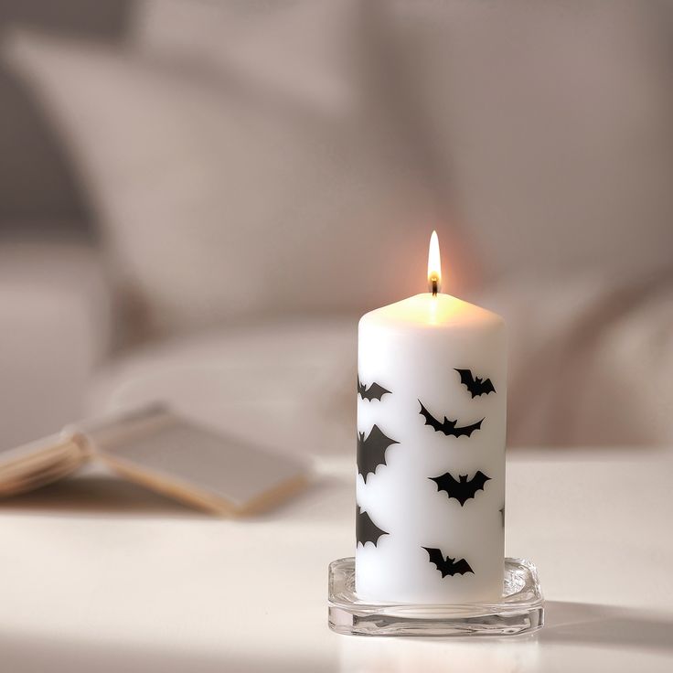 a white candle with black bats on it next to a cell phone and a book