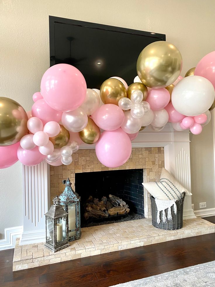 a fireplace decorated with pink, gold and white balloons