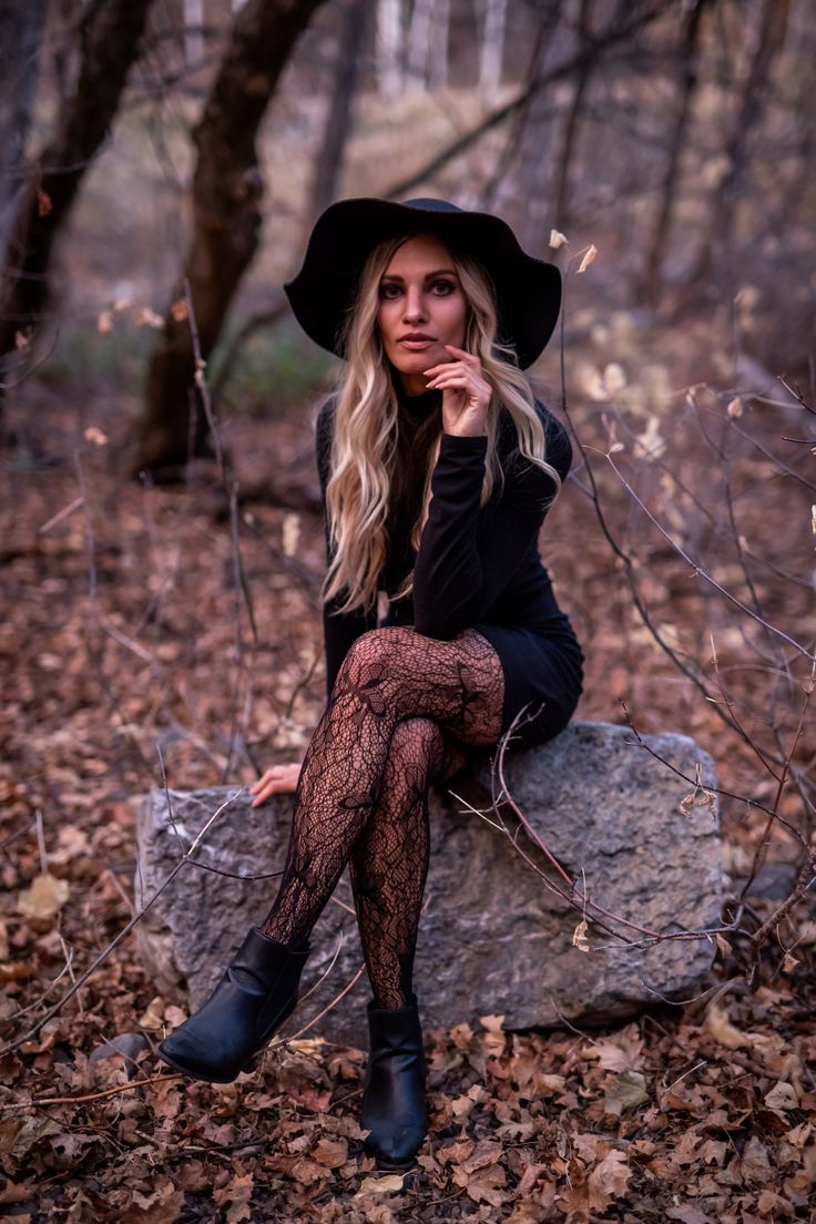 a woman sitting on top of a rock in the woods wearing a black hat and stockings