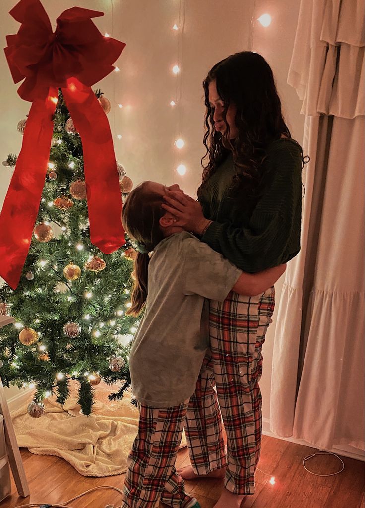 a woman holding a child in front of a christmas tree