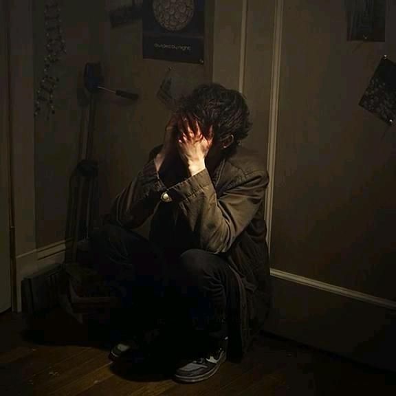 a man sitting on the floor in front of a door with his hands to his face