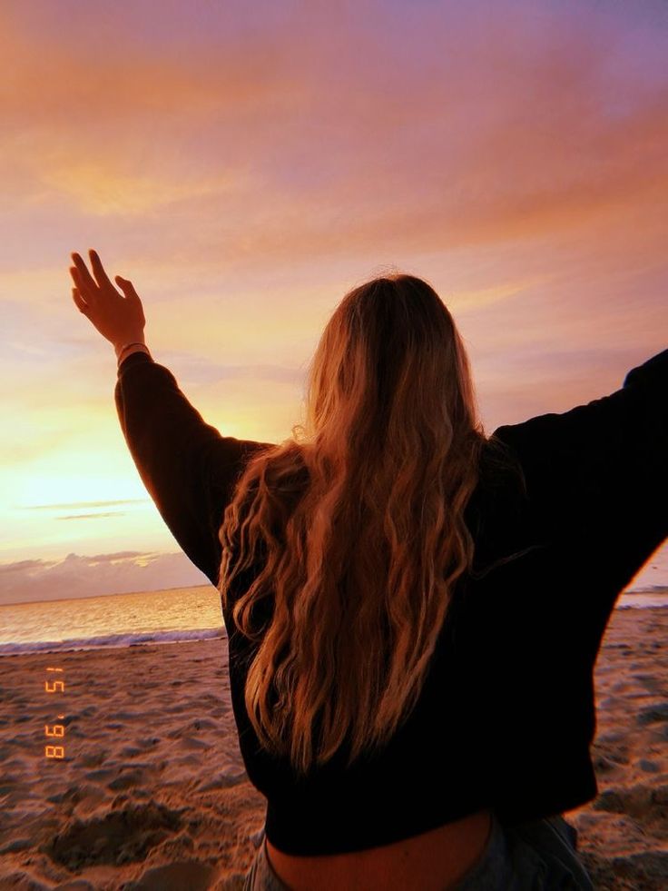 a woman standing on top of a sandy beach next to the ocean holding her arms in the air