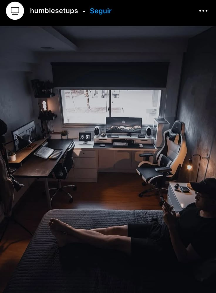 a man sitting in front of a computer on top of a desk next to a window