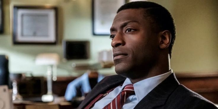 a man in a suit and tie looking off into the distance while sitting at a desk