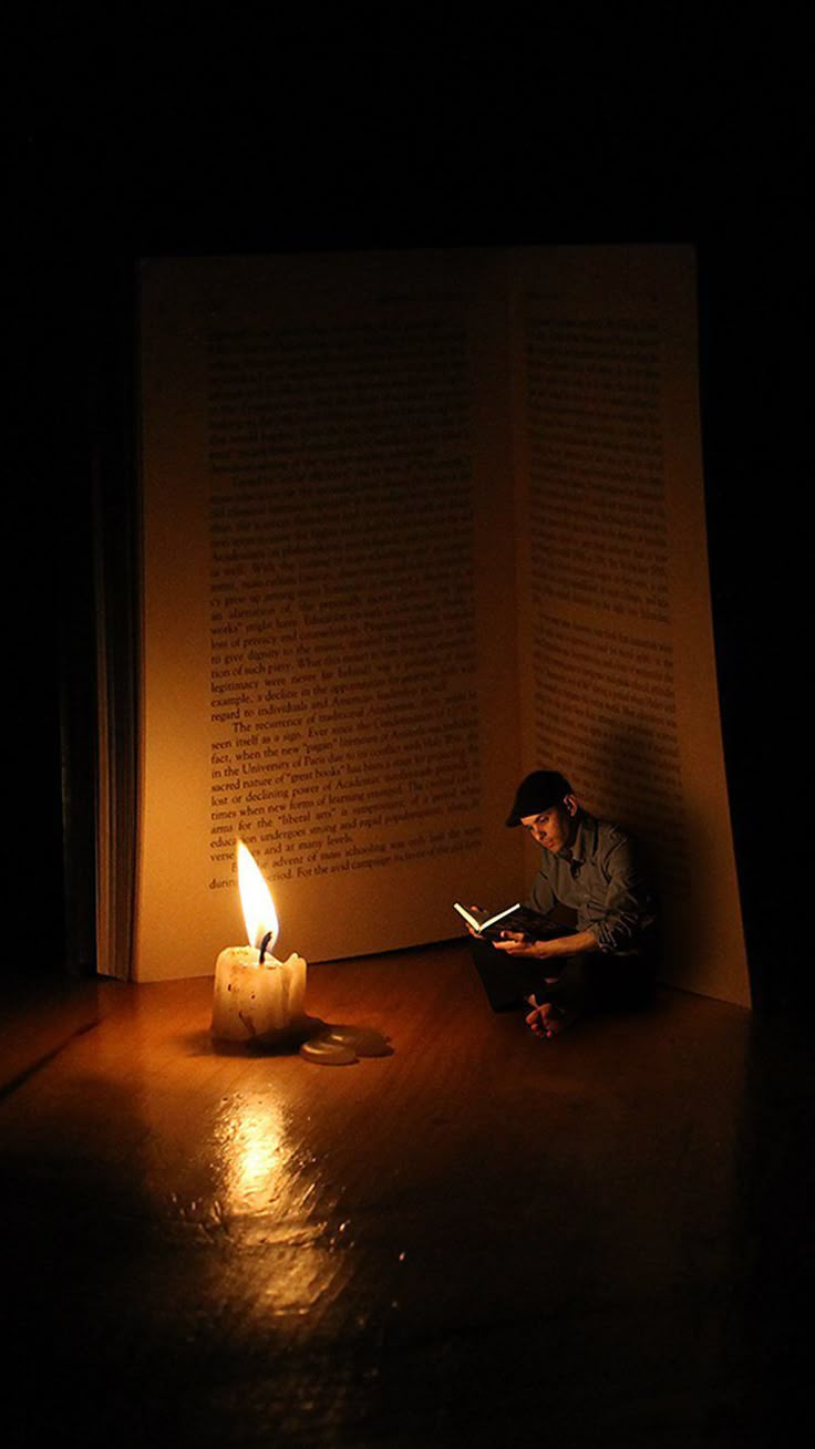 a man sitting on the floor reading a book with a lit candle in front of him