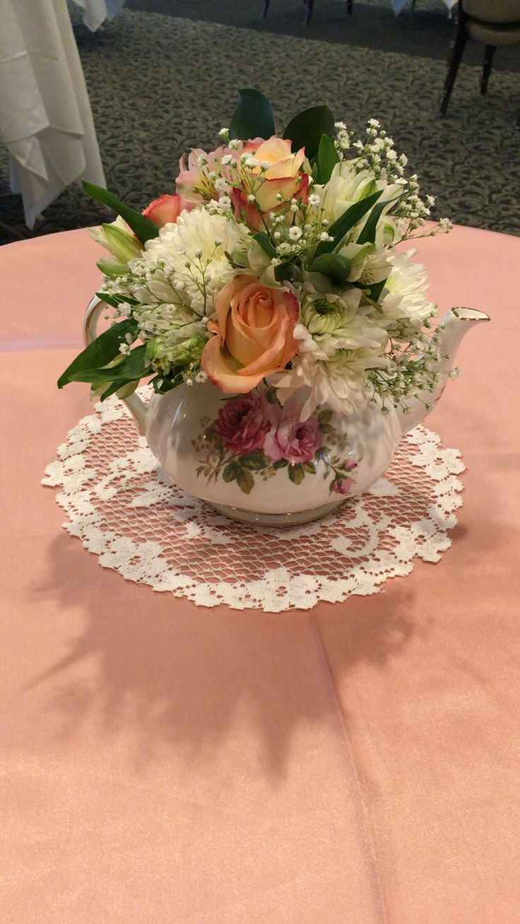 an arrangement of flowers in a teacup on a table with doily at the center