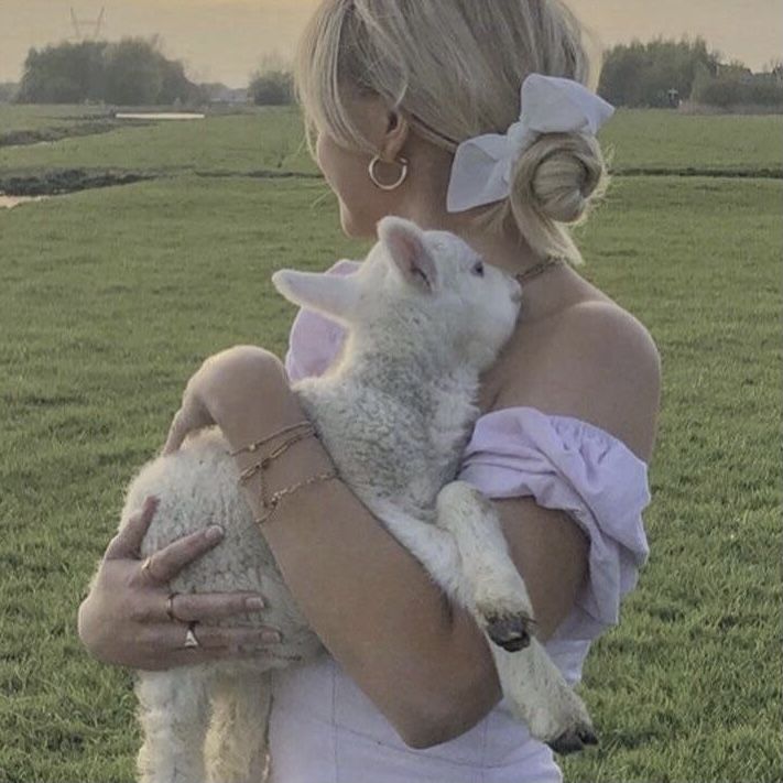 a woman is holding a lamb in a field