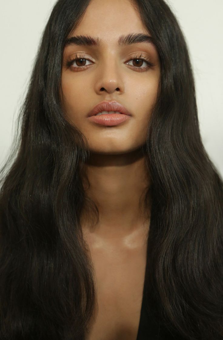 a woman with long black hair and brown eyes looks at the camera while wearing a black top