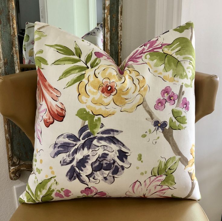 a floral pillow sitting on top of a wooden chair next to a mirror in a room