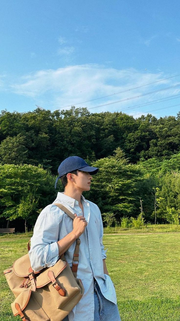 a man in a hat and blue shirt carrying a tan duffel bag on his shoulder