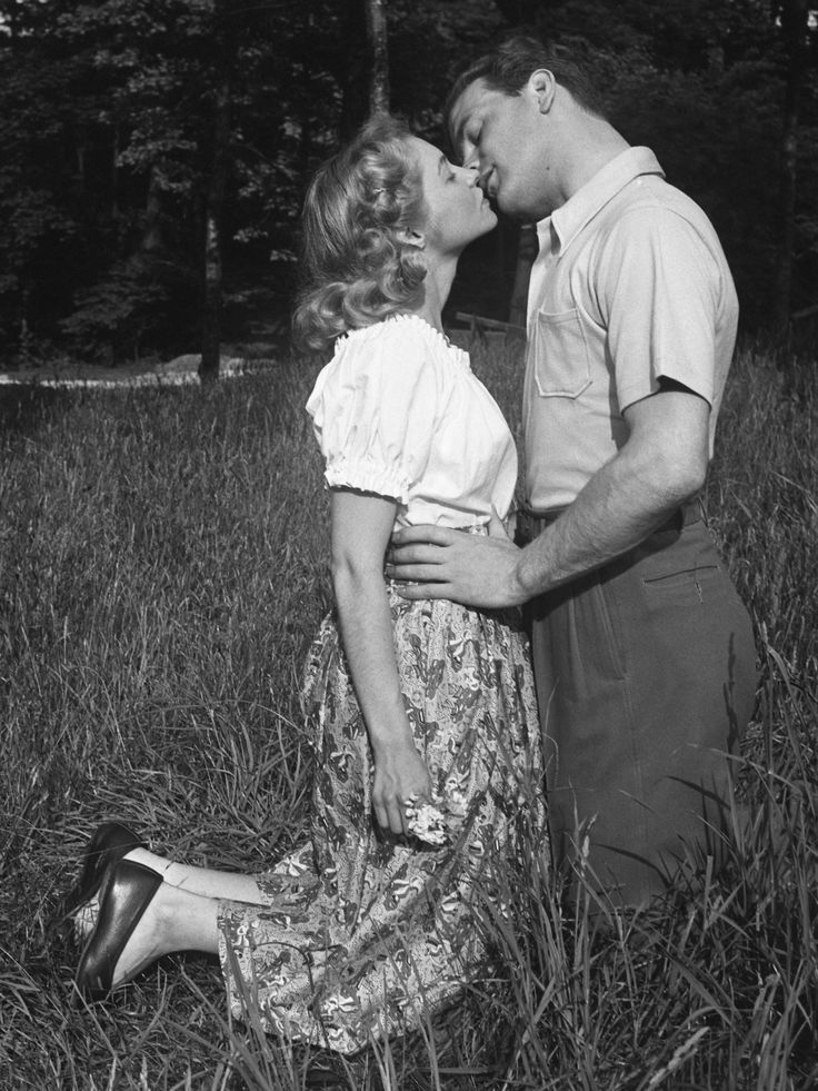 an old black and white photo of a man kissing a woman on the cheek in a field