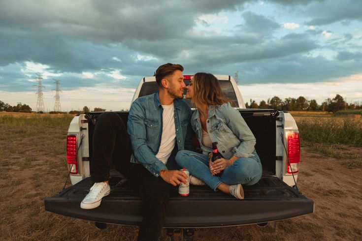 a man and woman sitting in the back of a pick - up truck, kissing