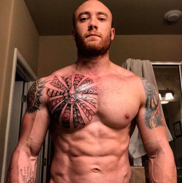 a man with tattoos on his chest standing in front of a mirror