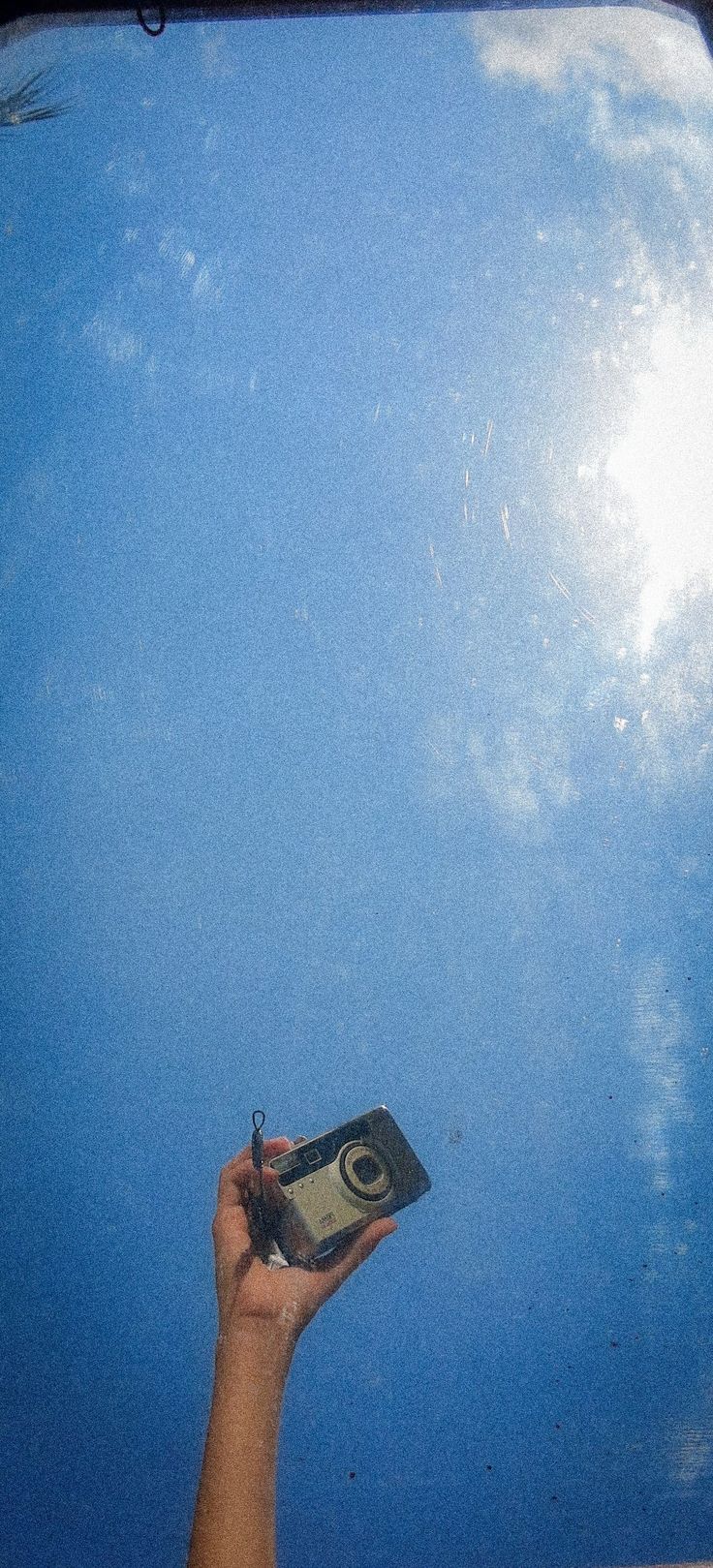 a person holding up a camera in front of a blue sky with clouds and sun