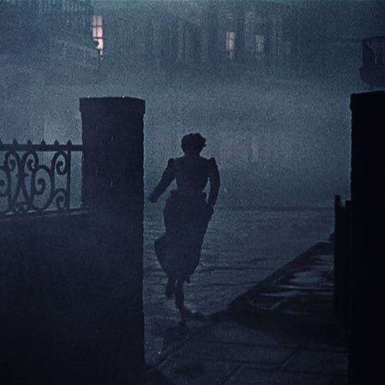 a woman walking in the rain at night with an umbrella over her head on a rainy day