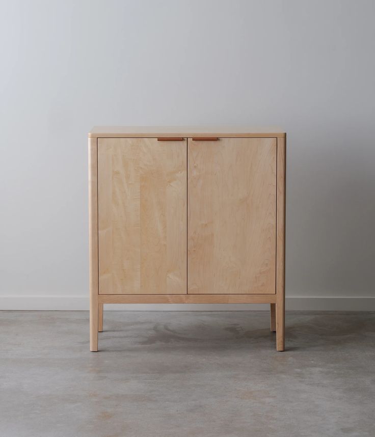 a wooden cabinet sitting on top of a cement floor next to a white wall in an empty room