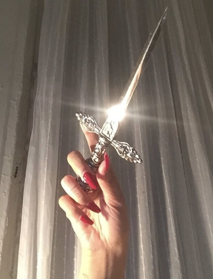 a person holding a cross in their hand with sunlight streaming through the curtain behind them